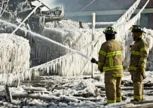 Firefighters battle an icy blaze, with water frozen mid-air by frigid temperatures, encapsulating the scene in a frozen cascade.